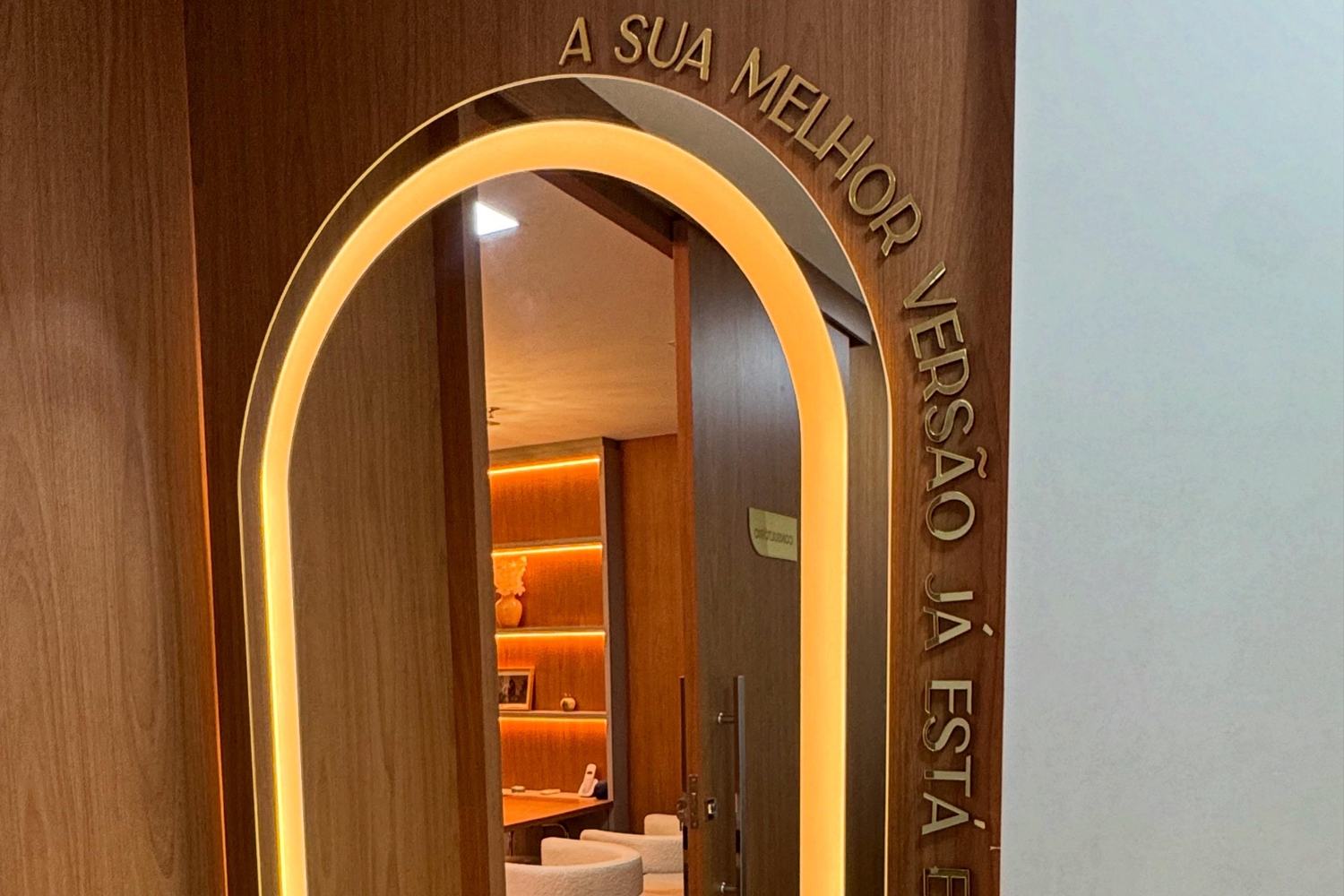 Espelho em arco iluminado na entrada, com a frase 